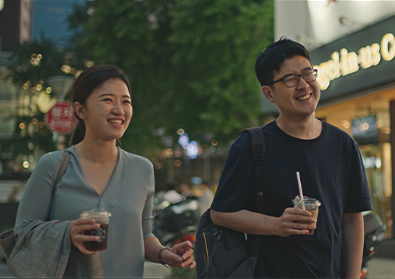 Founders, Suji and Han, are walking with drinks in their hands along a dimly lit sidewalk.